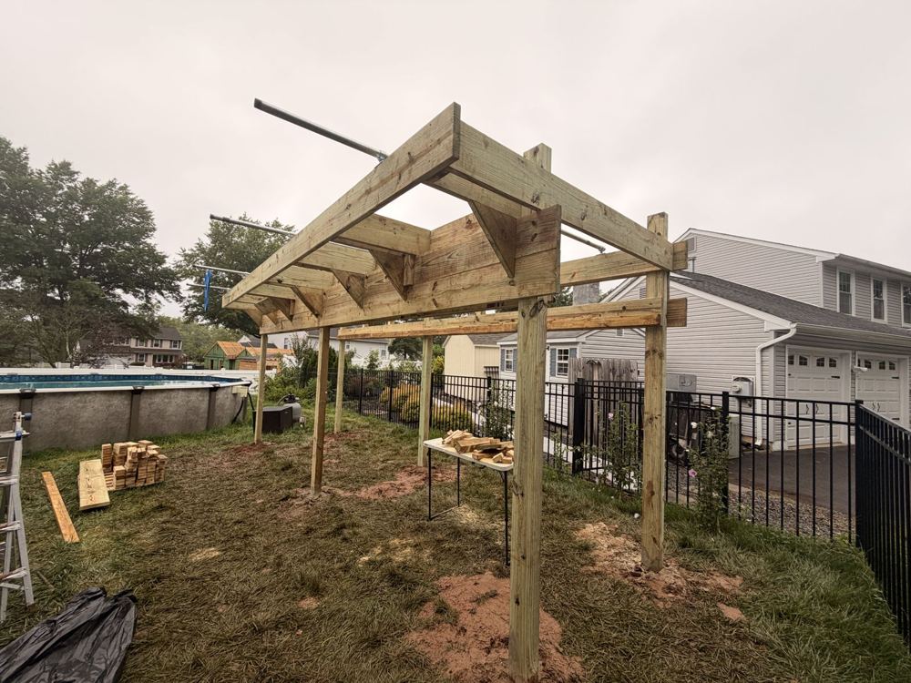 Unstained ninja rig frame taking shape in a fenced backyard next to a pool